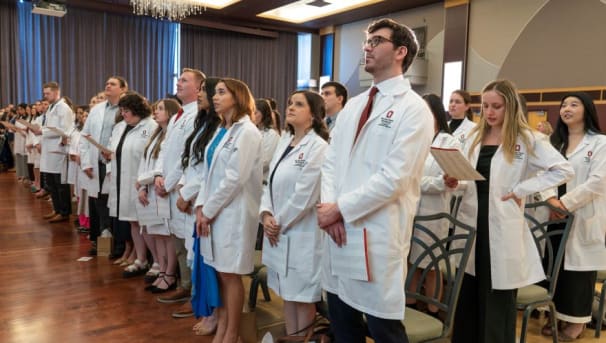 Audience of people in white coats standing with hands clasped