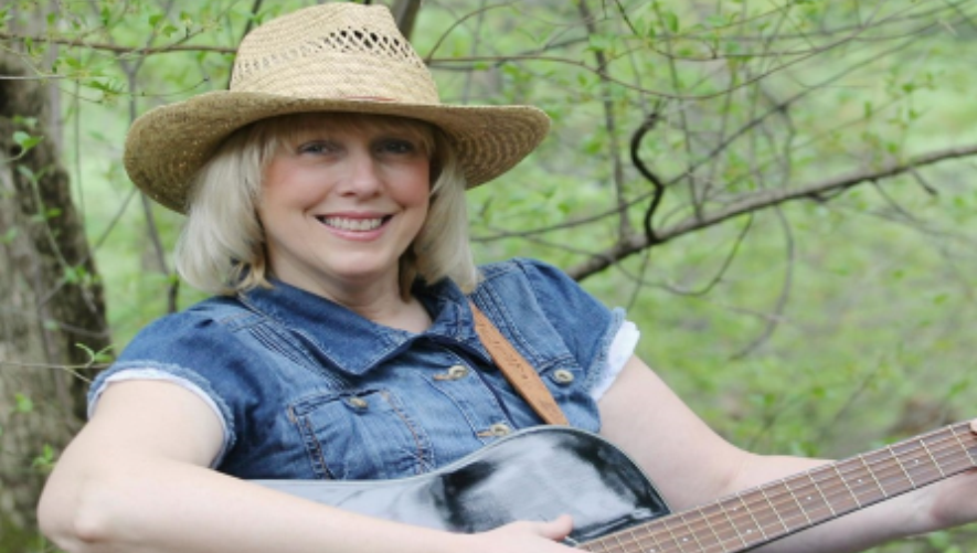An individual with a blonde bob sitting outdoors, holding a black and white guitar.