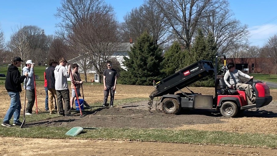Students with rakes watch as soil is dumped