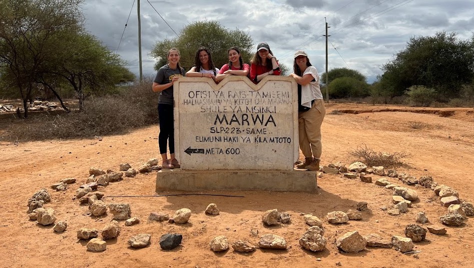 Five individuals standing behind a large concrete sign that says Marwa