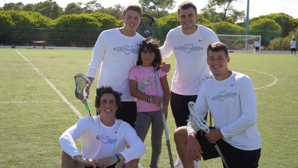 Four Ohio State Men's Lacrosse players pose with a young girl on a lacrosse field