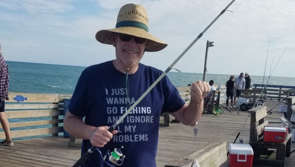 Individual wearing a hat while fishing on a pier. He holds a fishing rod in both hands