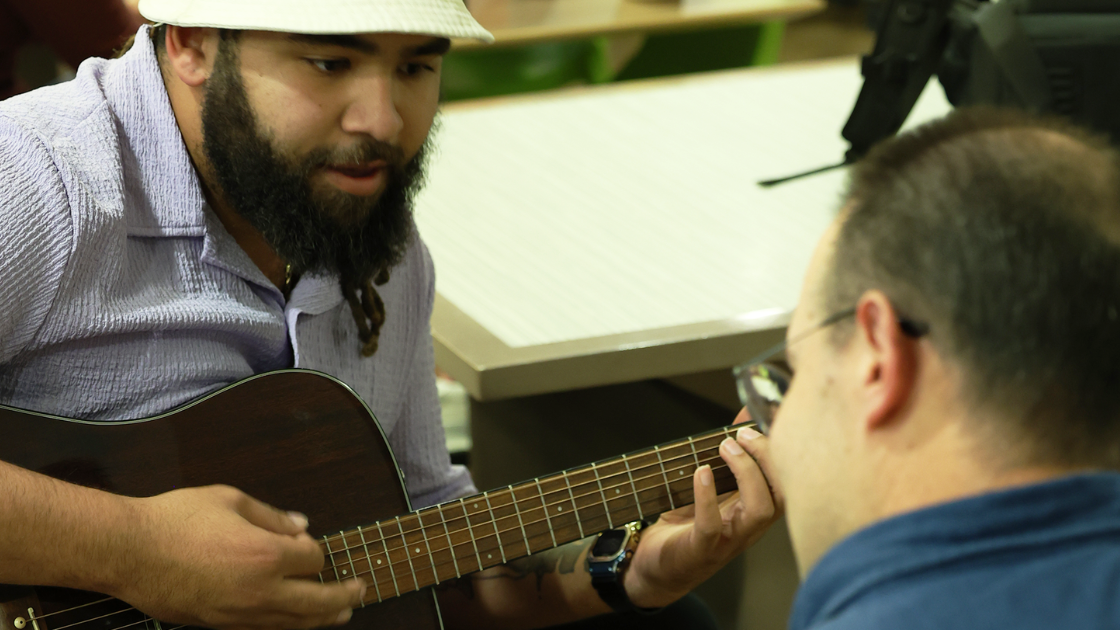Student taking instructions from professor on how to play a guitar.