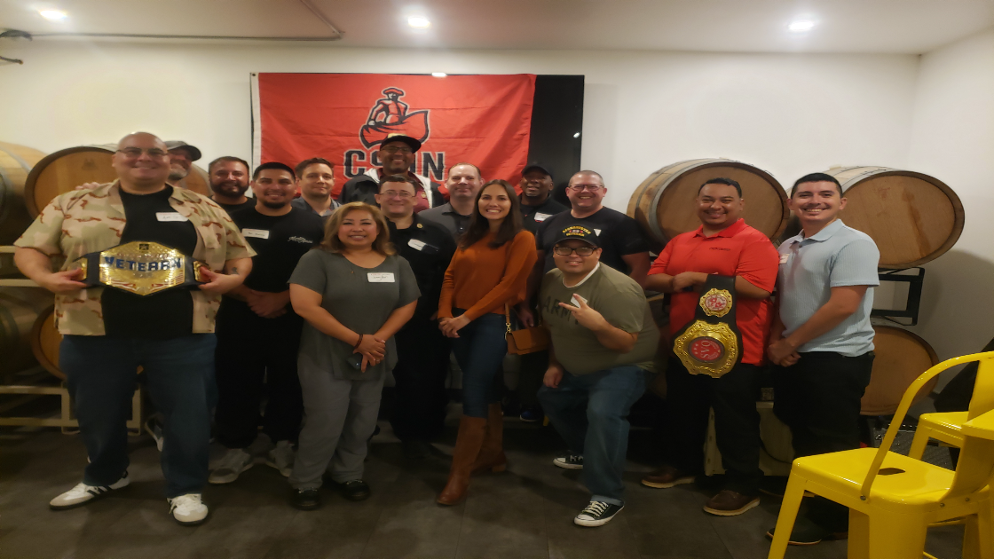 CSUN veterans alumni group posing indoors with banner and championship belts.