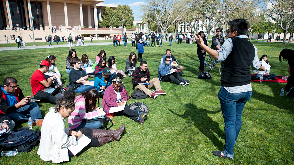 Instructor leads an outdoor class on the CSUN lawn with students seated and taking notes.