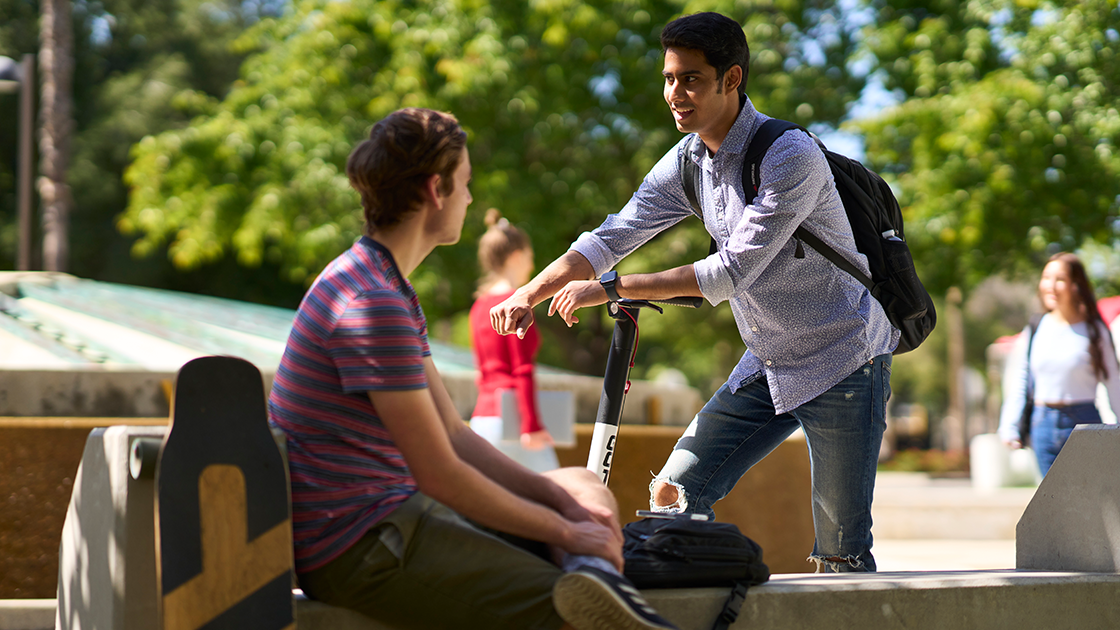 Student with skateboard and scooter talking.