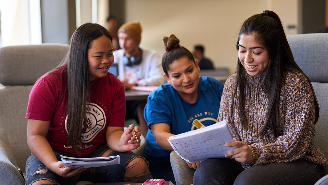 Three students looking at a notebook working on a project.