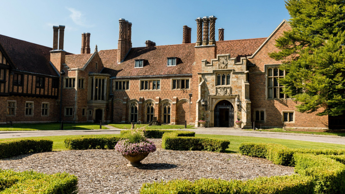 The exterior of Meadow Brook Hall - a large brick building - with shrubs and flowers in the fron.