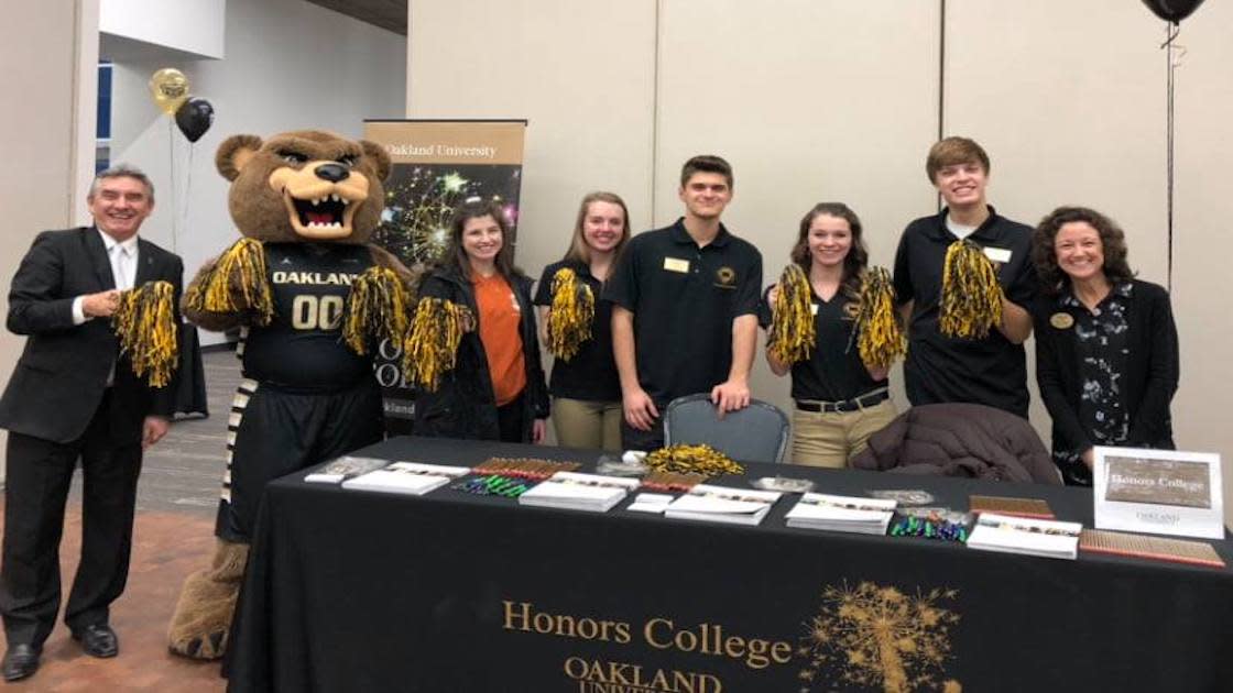 Honors College students pose with Grizz in front of an Honors College Table at an event.