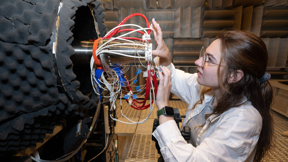 A researcher adjusts a cluster of cables and sensors connected to a large piece of equipment