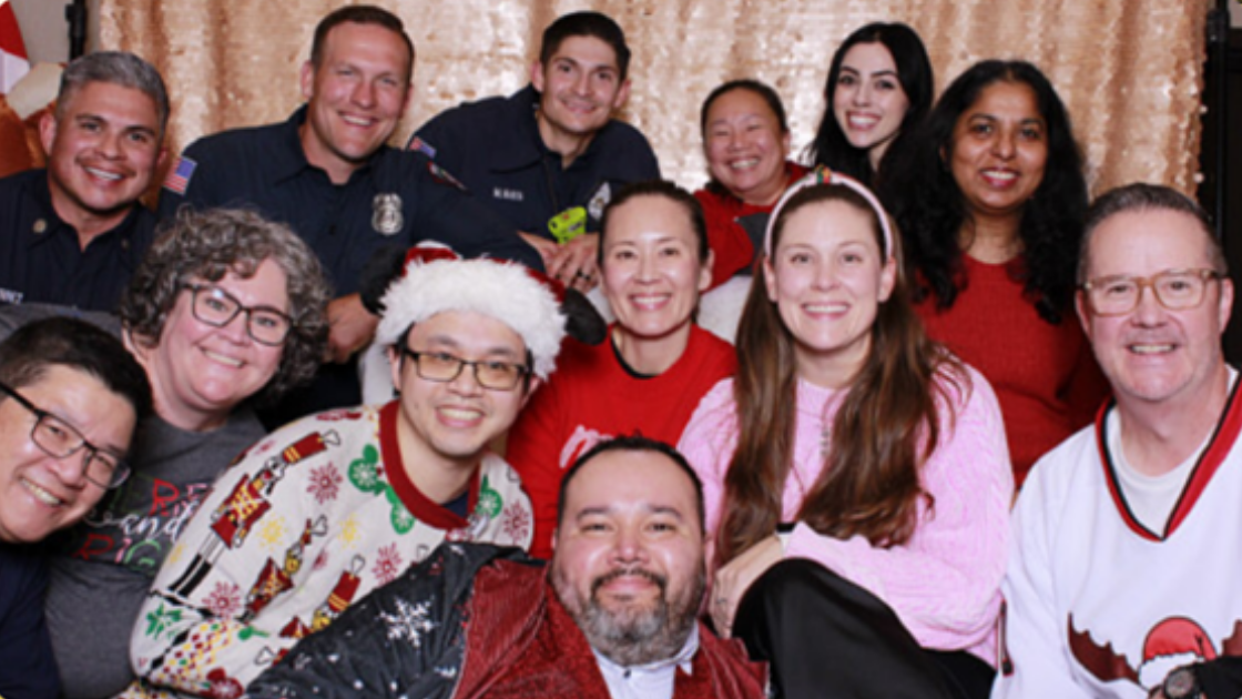 Cheerful group of UCI Health staff and local firefighters posing in festive holiday attire