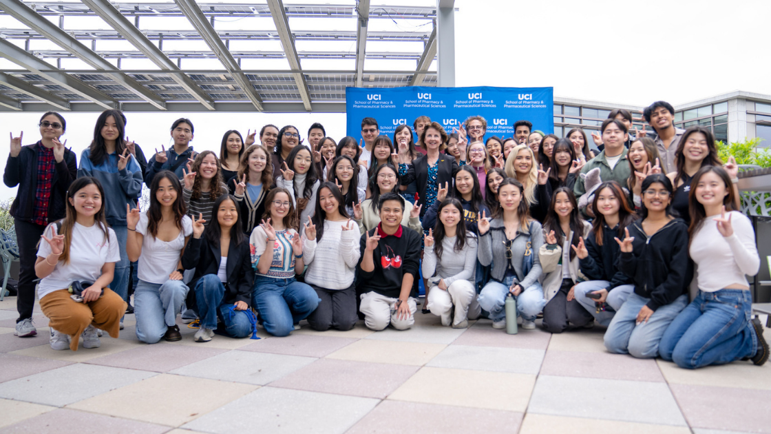 Students pose in front of a logo wall at an event, all holding the "zot" hand sign