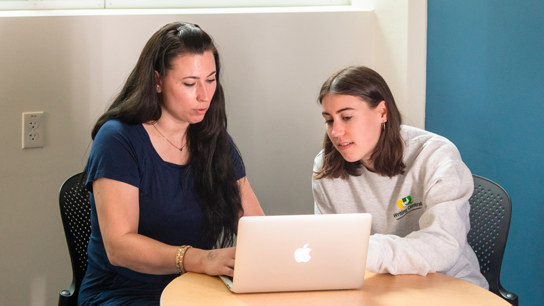 Two SOJC students sit around a laptop, working together on a group project.