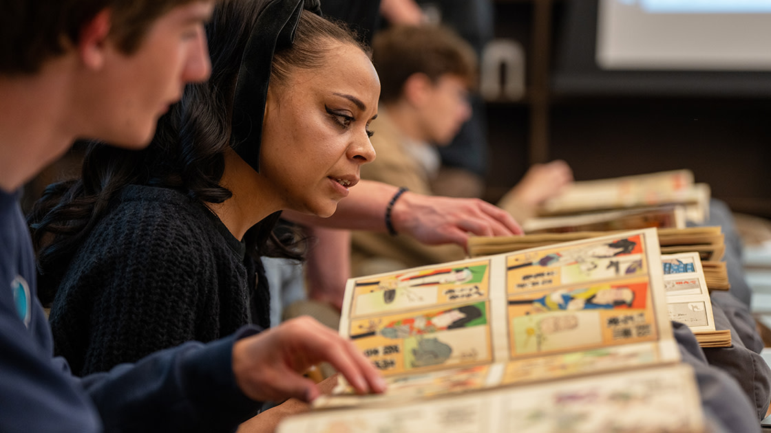 A woman with light brown skin looking a book of vintage Japanese prints