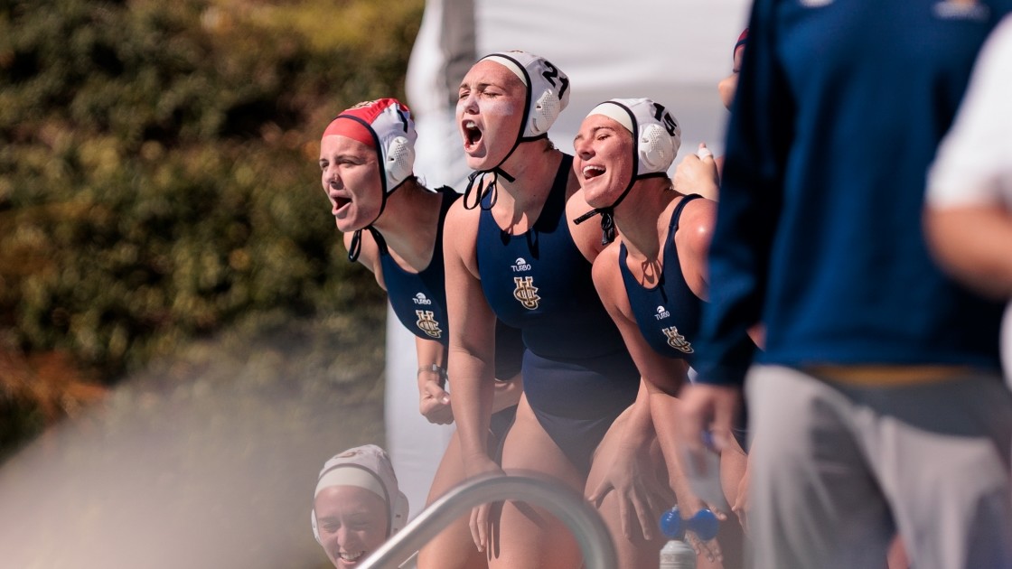 Three UCI women's water polo players cheering from the sidelines of the pool during a match