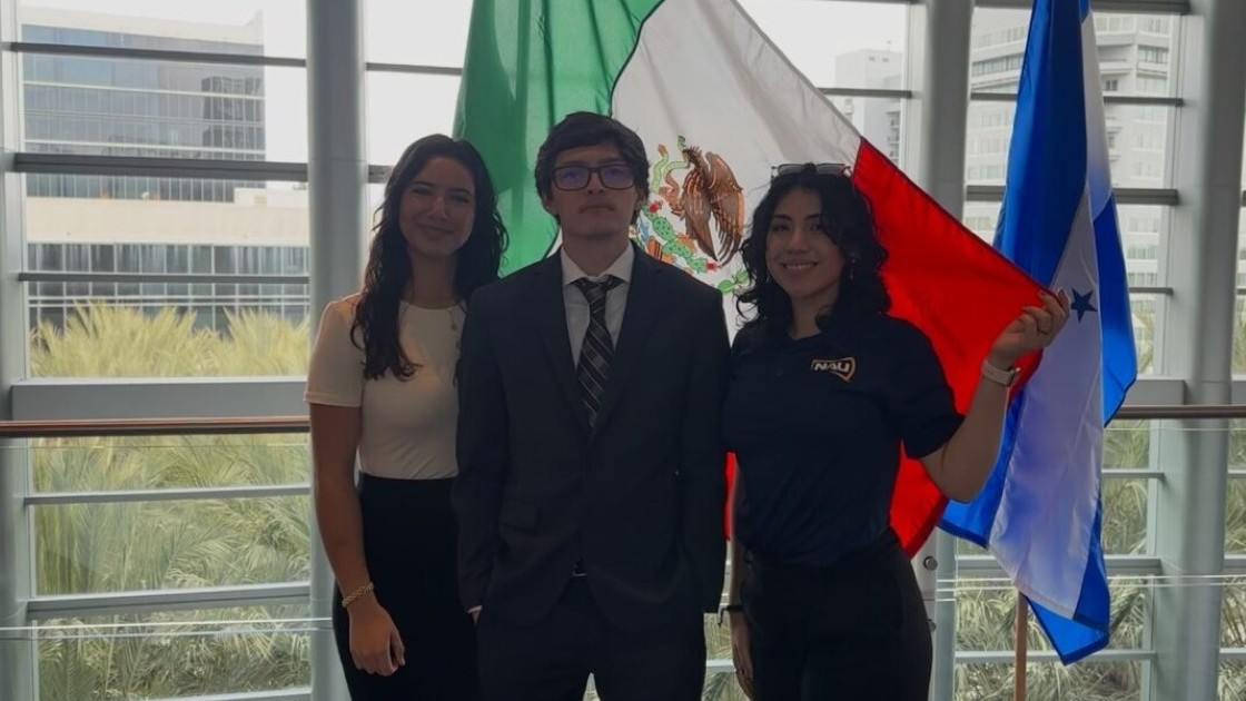 Three officers stand in front of the Mexican flag.