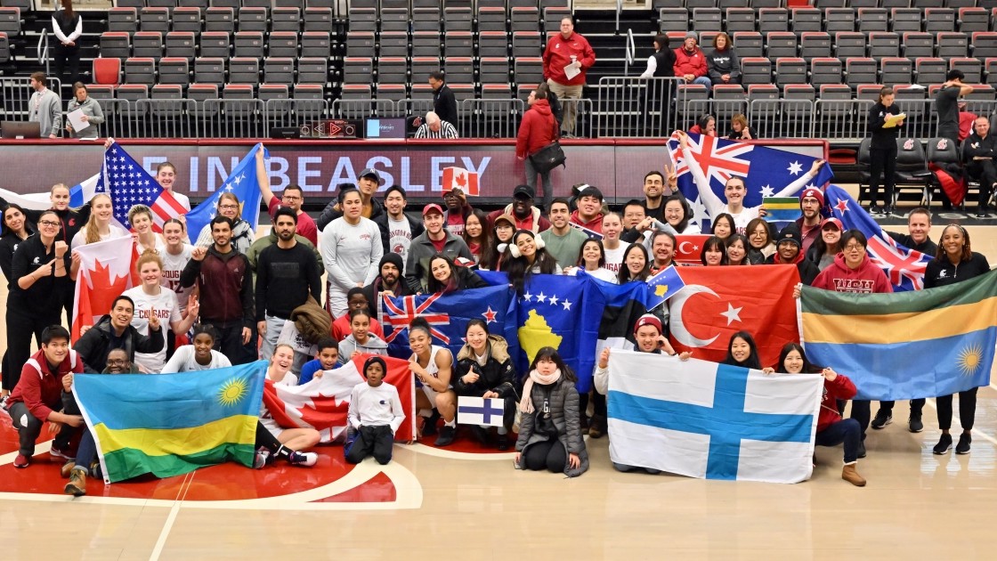 International students posing with flags at a basketball game