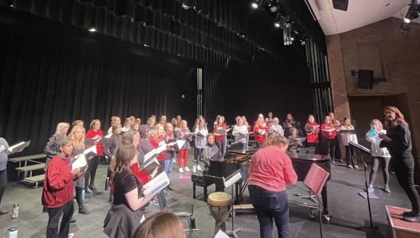 Women's Glee Club members rehearsing on a stage led by their conductor