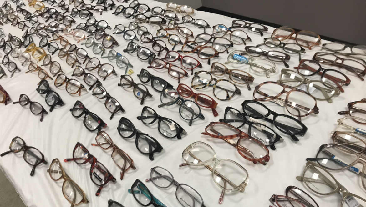 Many rows of prescription glasses line a white clothed surface