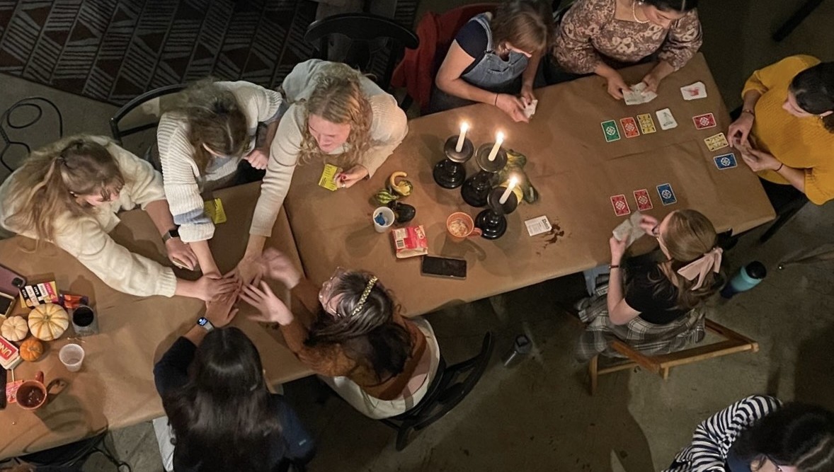 Members of Women's Glee play cards around a table at "Thanksgleeving"
