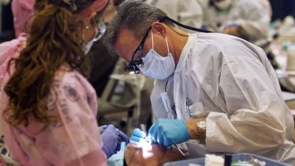Two nurses bent over a patient's open mouth