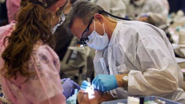 Two dentists stand by a patient. One holds a flashlight and looks into the patient's mouth