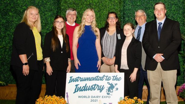 A group of professionally dressed individuals posed around the 'Instrumental to the Industry' sign.