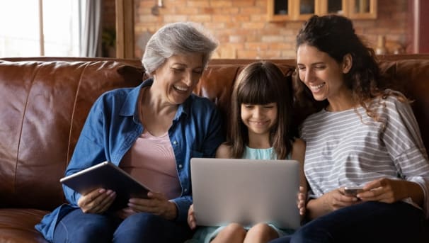 grandmother, grandchild and mother all sitting together around a laptop learning