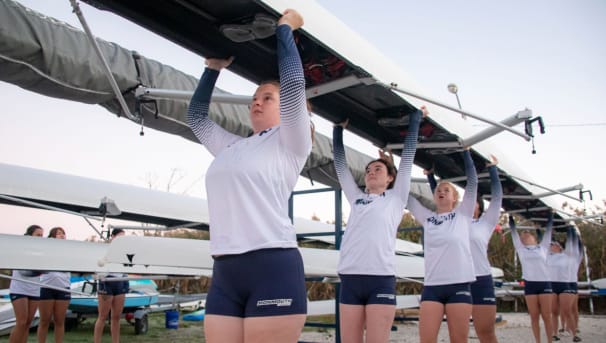 Monmouth Rowing student-athletes carrying an eight-person boat into the water for competition.