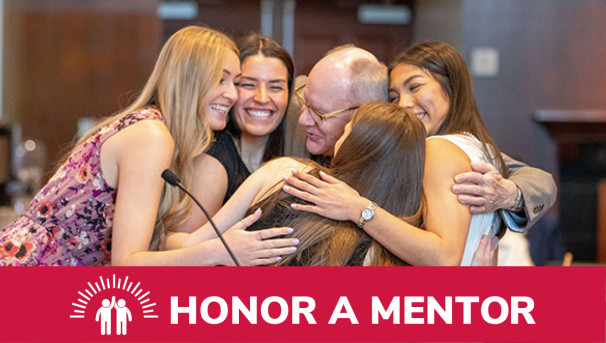 A group of smiling students at a podium embracing their professor