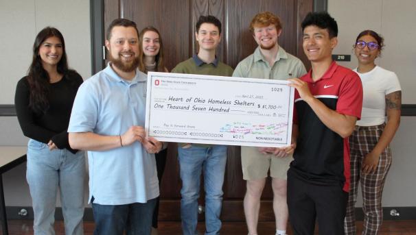 Seven students standing in a room holding an oversized check
