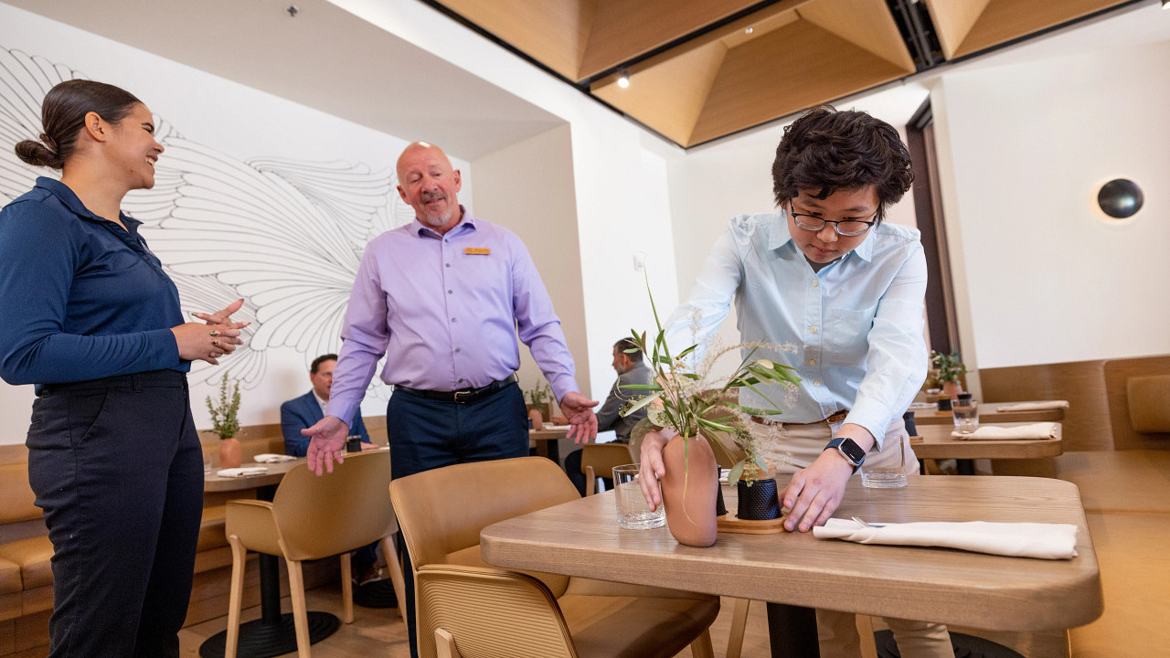 Student setting up a table with two instructors behind them.