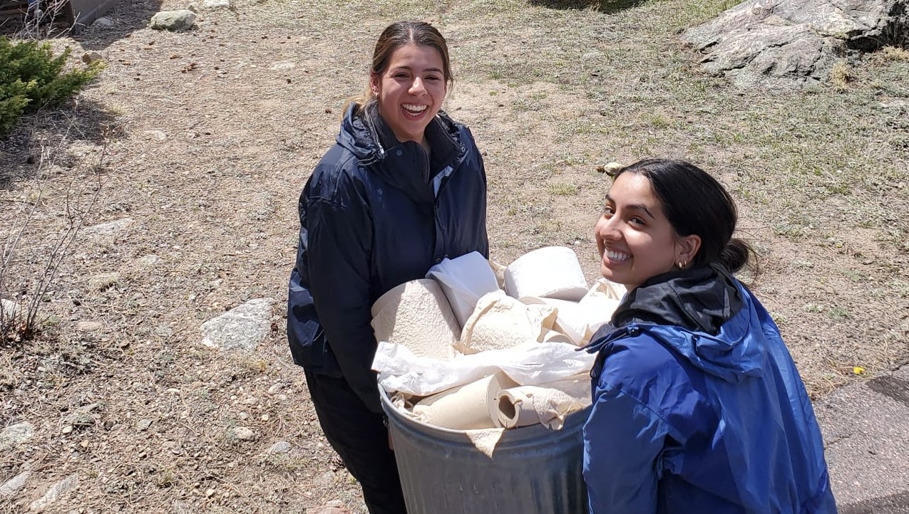 2 students holding bucket of paper towels outside