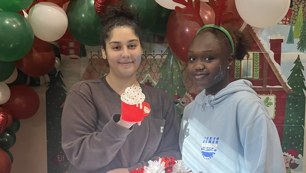 Two individuals smiling for a photo in front of a Christmas background