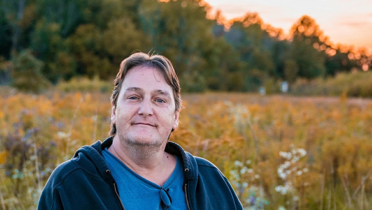 Jon sitting before a field and an orange sunset