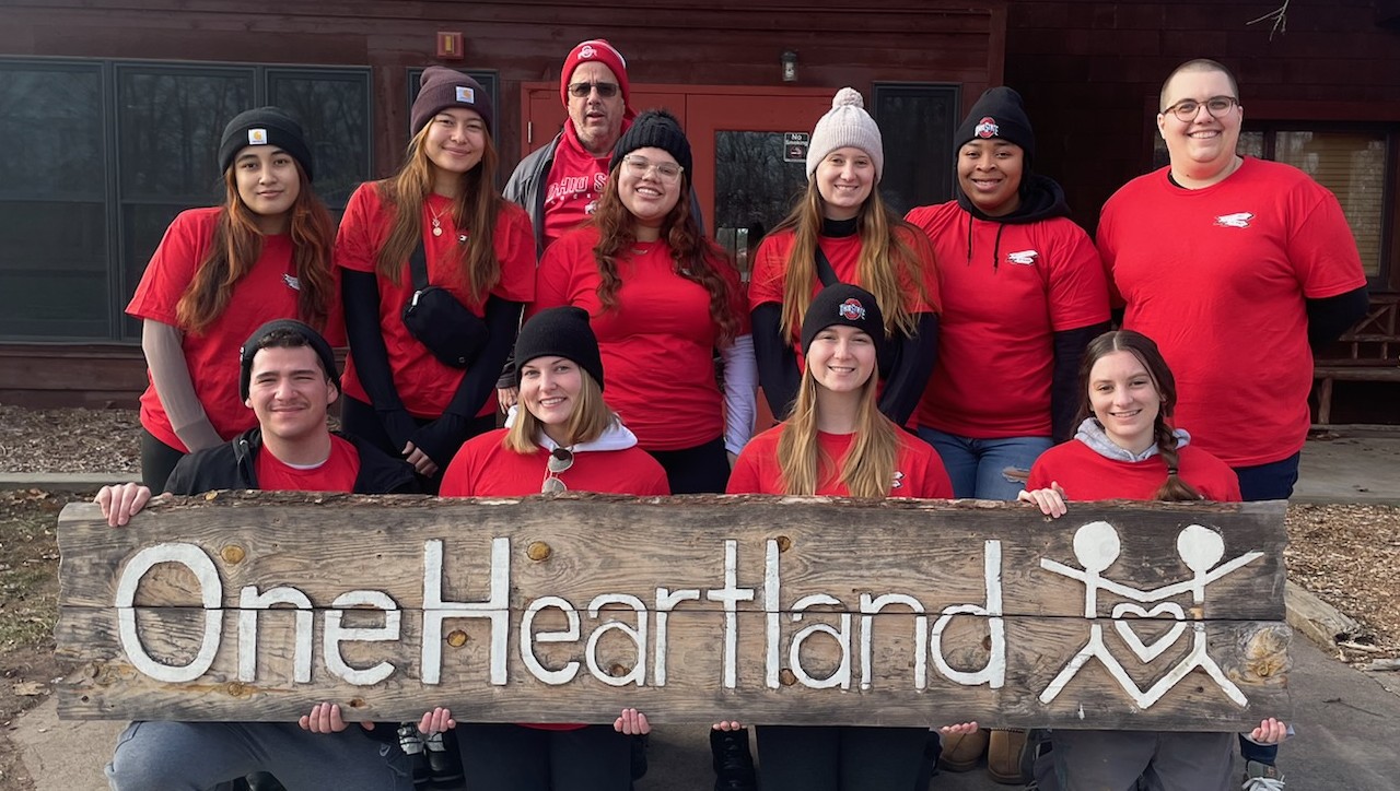 Group of individuals outside holding a sign that says One Heartland camp