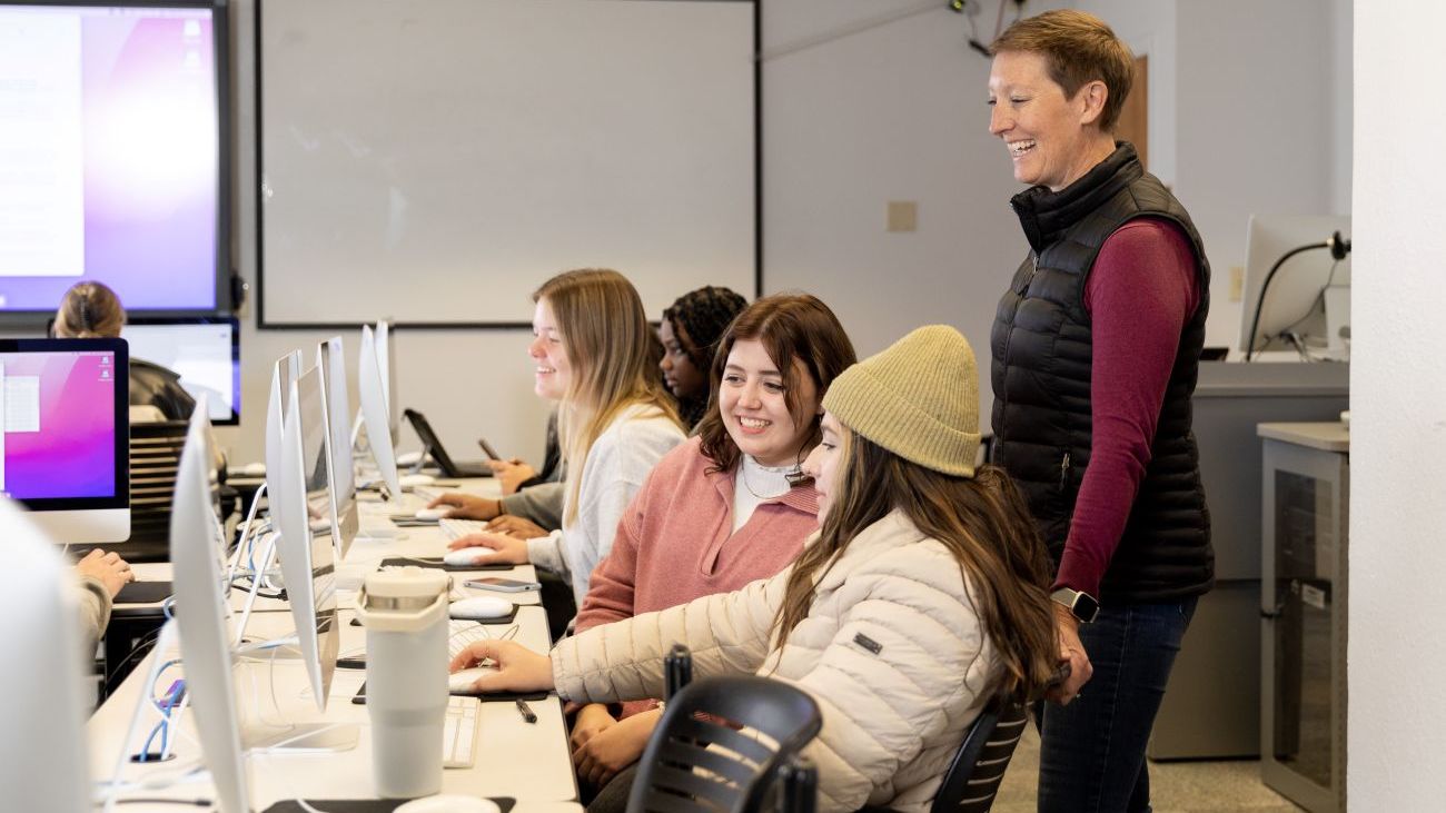 An instructor assists students as they work on computers in a design class.