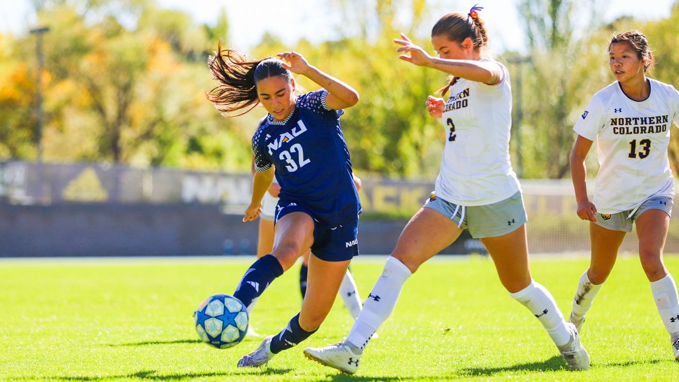 NAU Women's soccer player #32 goes towards the ball, faces an opposing player on the field.