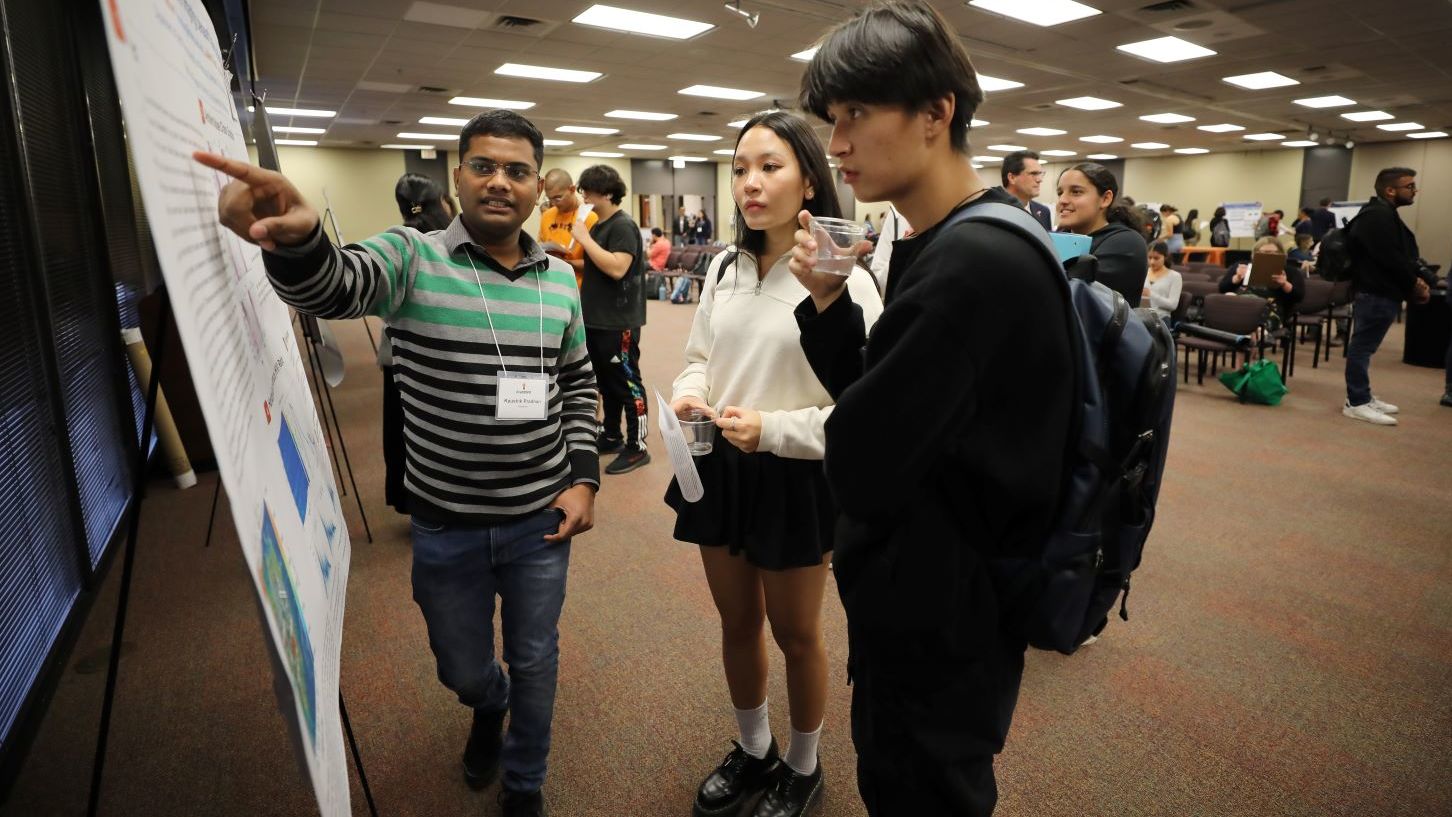 Graduate student presenting poster to two other individuals