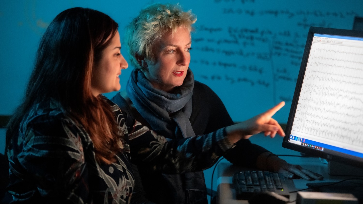 Student pointing to a screen displaying jagged line graphs while speaking to the professor