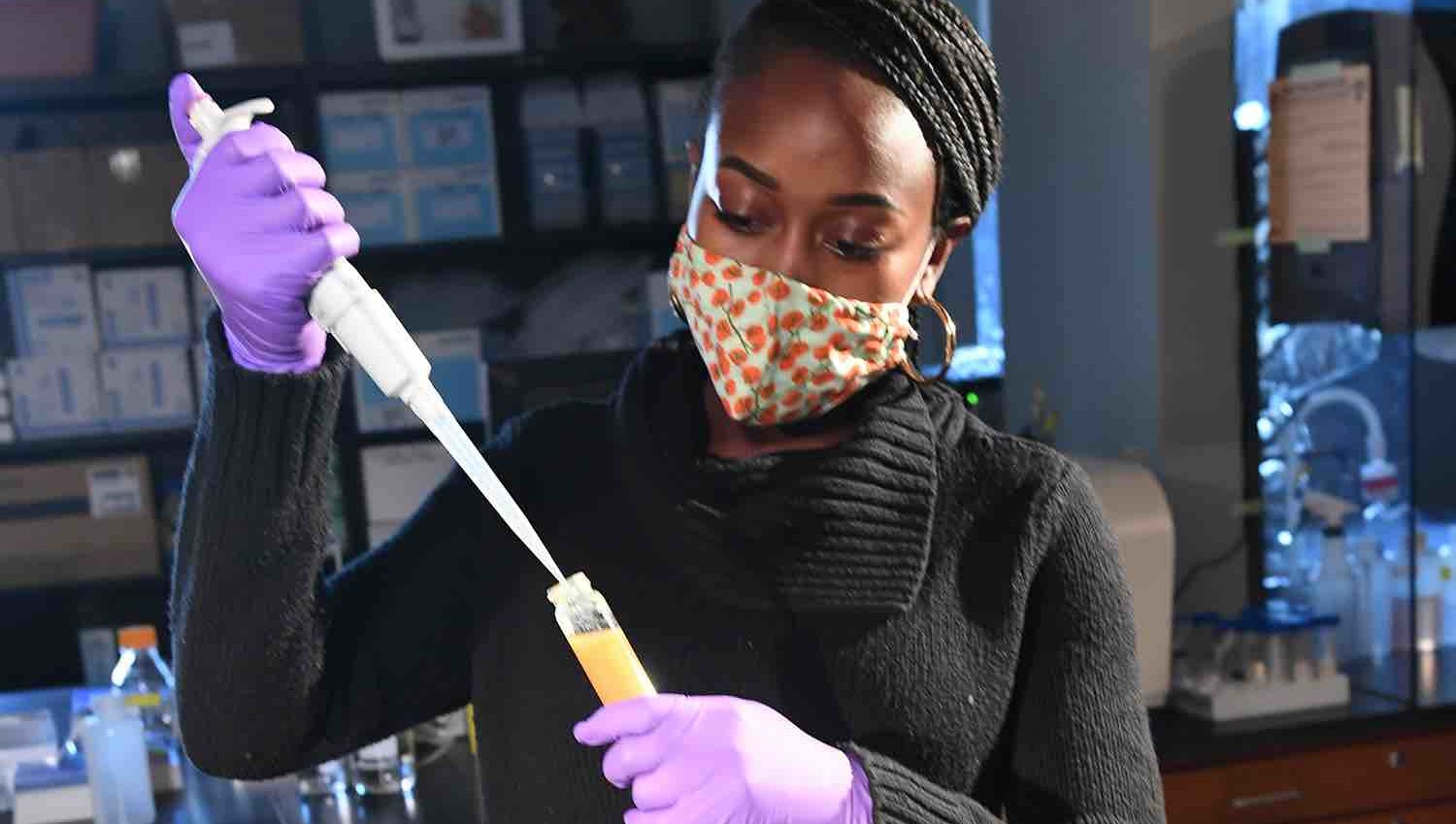 A woman in a black sweater holds a pipette and tube at the Jessica Cooperstone Lab