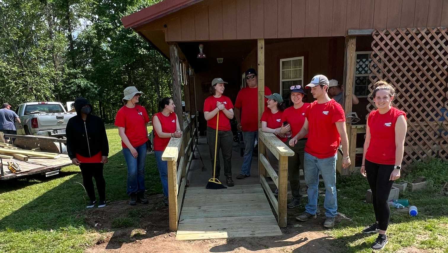 Nine volunteers stand near a house porch, talking with one another