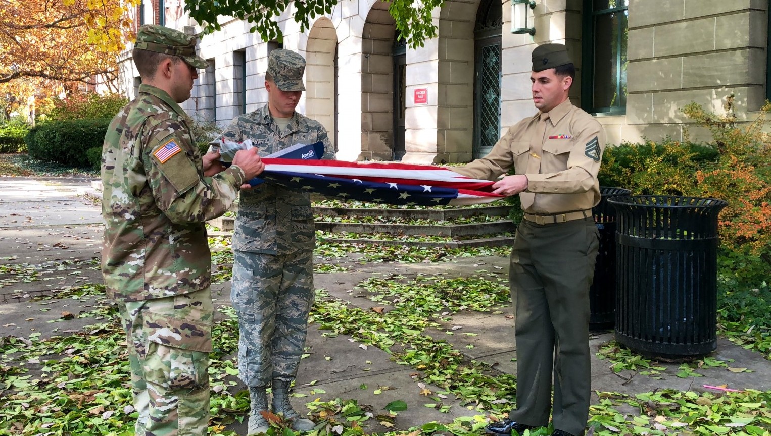 Three soldiers folding an American flag outside Bricker Hall