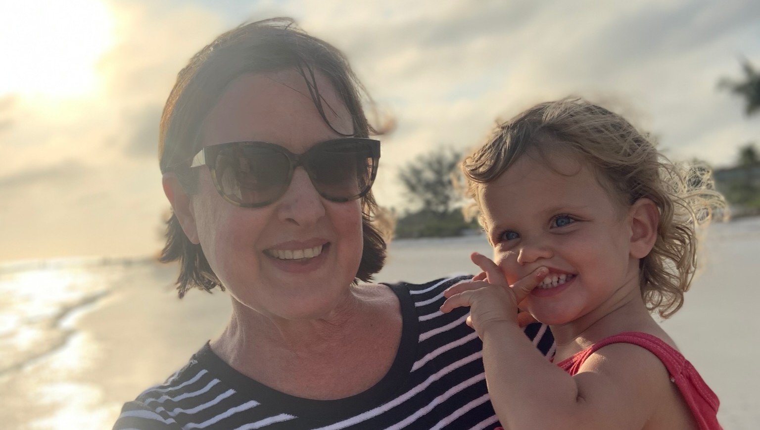 Becky Bennett holding a young girl with the ocean and beach behind them