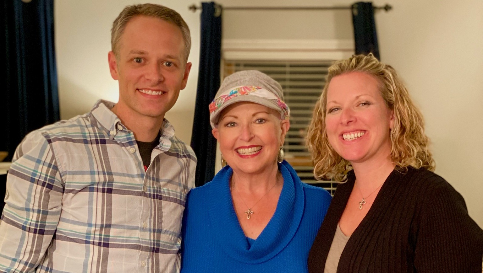 One man and two women smiling towards the camera. The middle woman wears a scarf on her head