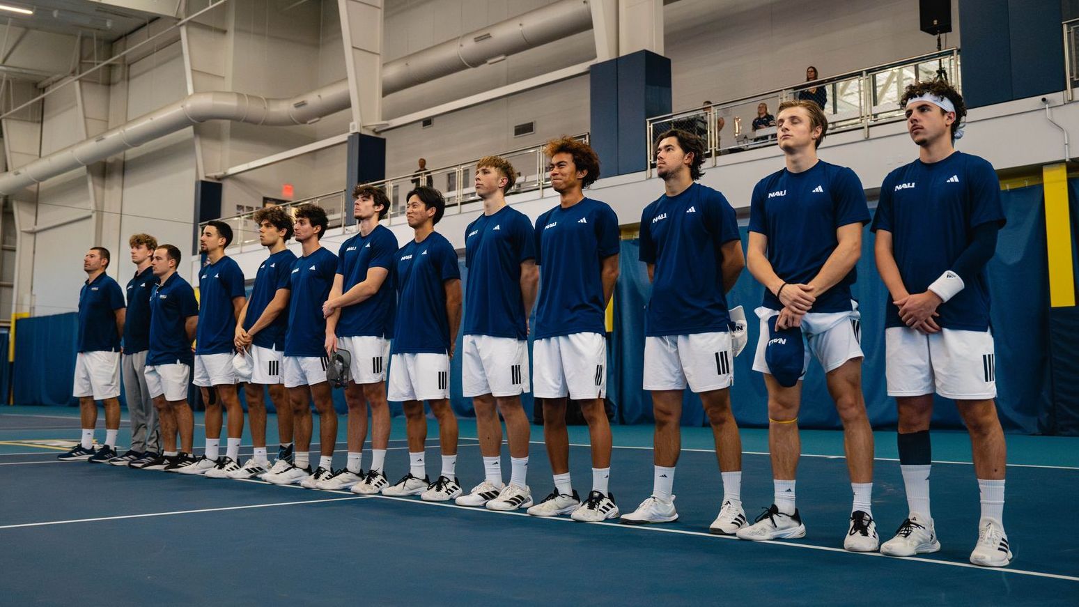 Men’s tennis team lined up on an indoor court.