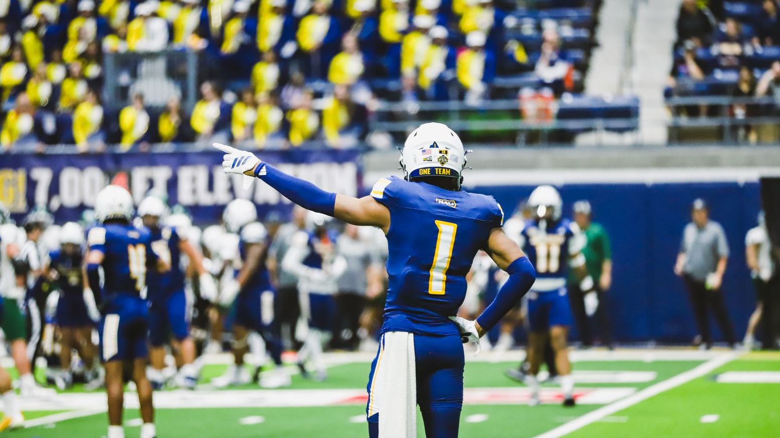 NAU Football player #1 points left and stands with hand on hip. Photo shows back of jersey.