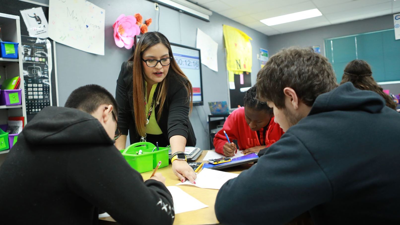 Elementary aged children sitting around a table while student teacher explains worksheet