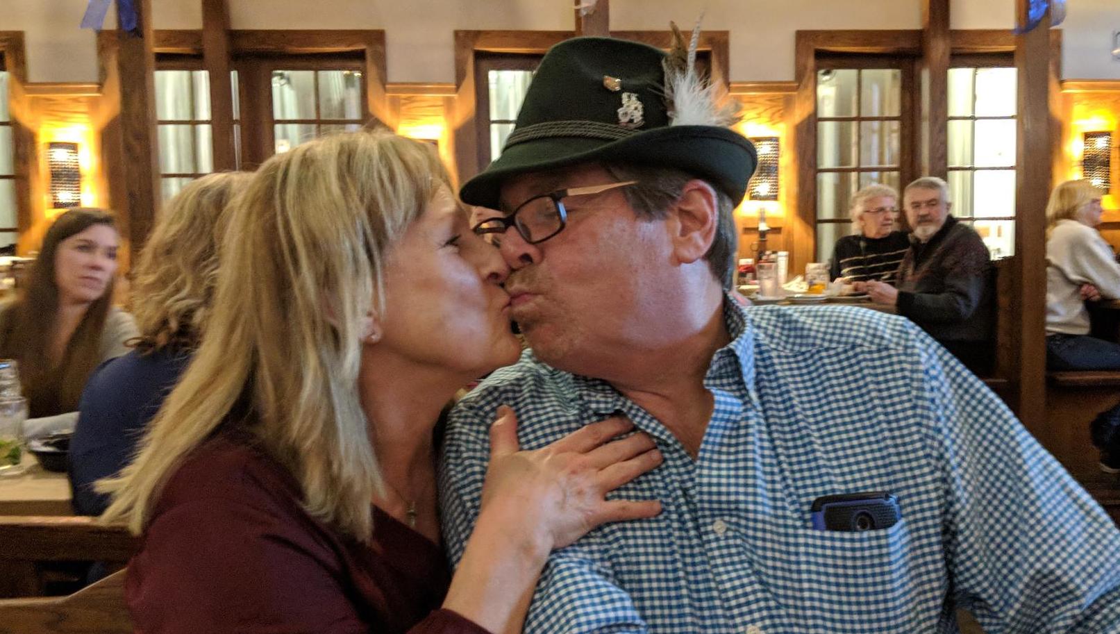 Two individuals giving each other a kiss while sitting down at a restaurant