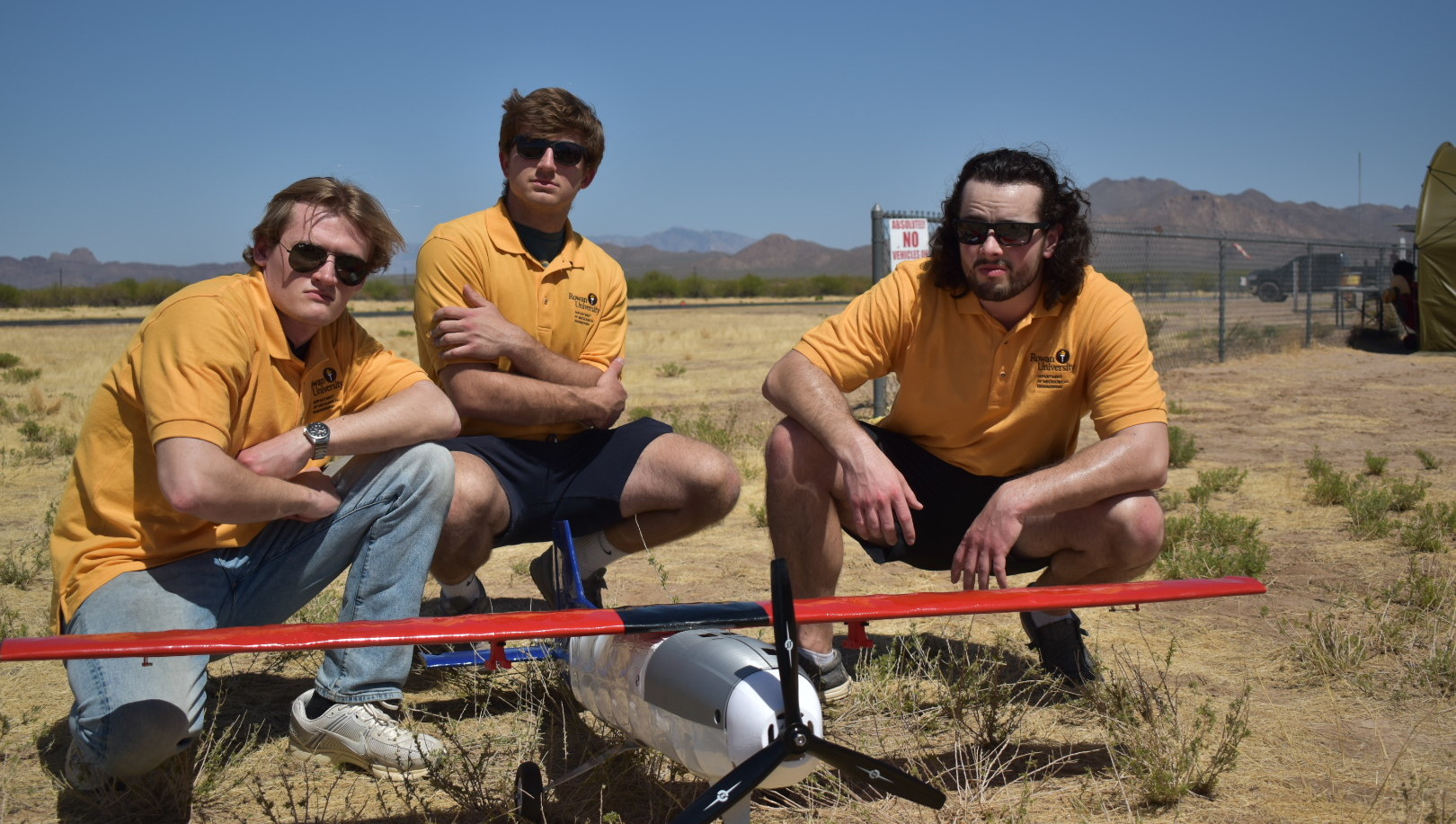 Three AIAA team members on location with plane on the ground in front of them.